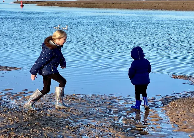 2 sisters splashing away on the edge of the sea in coats and wellies