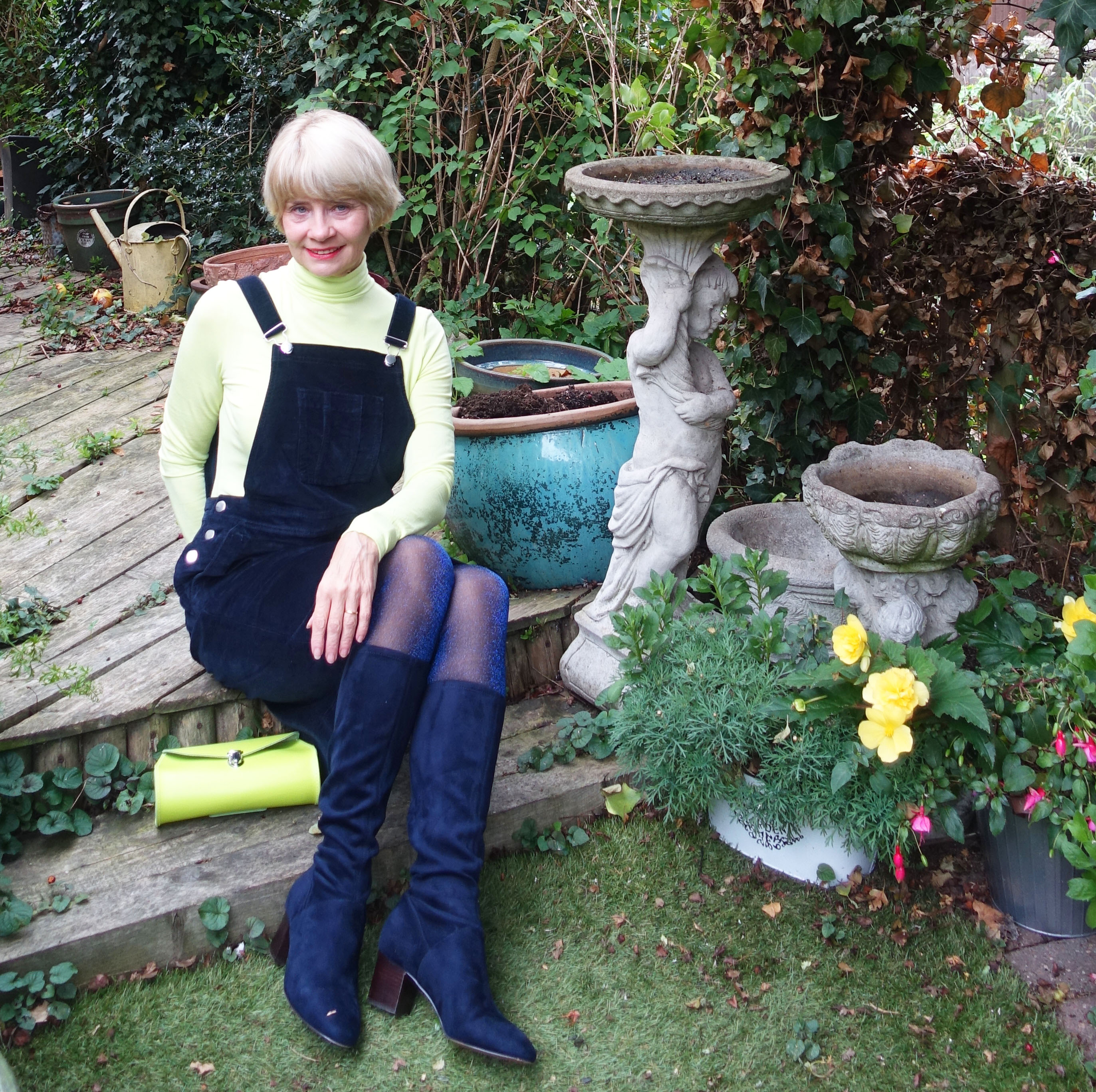 A navy cord pinafore from Cotton Traders styled with a silky roll neck in acid yellow and long blue boots from Boden.