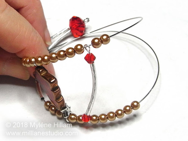 Two coils of memory wire strung with a hollow tube component and glass pearls.