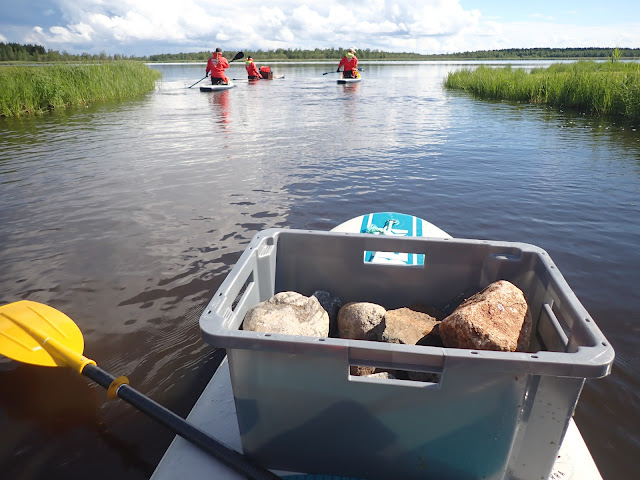 Henkilöitä pelastautumispuvuissa sup-laudoilla, mukana työvarusteita