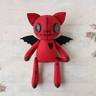 A photograph of a red and black, stuffed demon cat toy with button eyes, created by Bucreshki.
