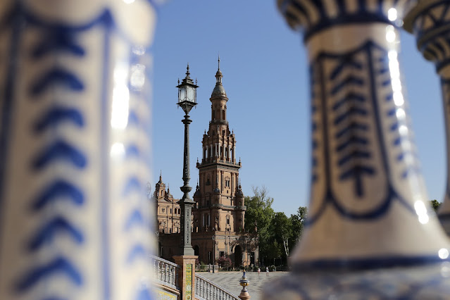 Una de las torres de la plaza de España de Sevilla entre los barrotes de una barandilla de cerámica.