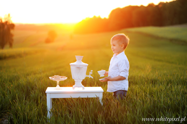 mały chłopiec na mazowieckich pagórkach o zachodzie słońca pozuje przy stoliku pije herbatę