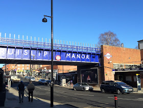 Pic of Ruislip Manor station and railway bridge with its name from opposite side of street