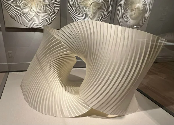 pleated abstract 3D paper sculpture on display and positioned in front of wall of three additional circular pleated paper sculptures
