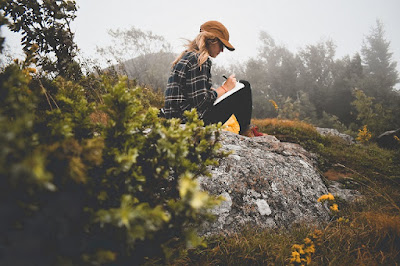 Woman sitting on a hill writing in a journal
