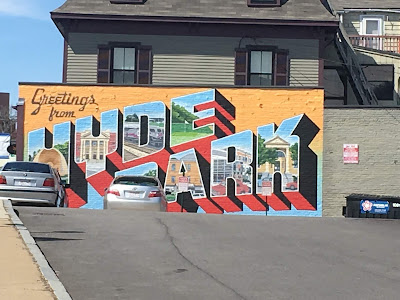 A mural that reads "Greetings from Hyde Park" with local scenes inside the letters. Two cars are obscuring part of the mural.