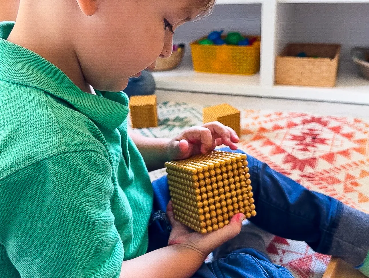 Three-year-old boy sits in his playroom at home counting Montessori golden bead thousand cube material