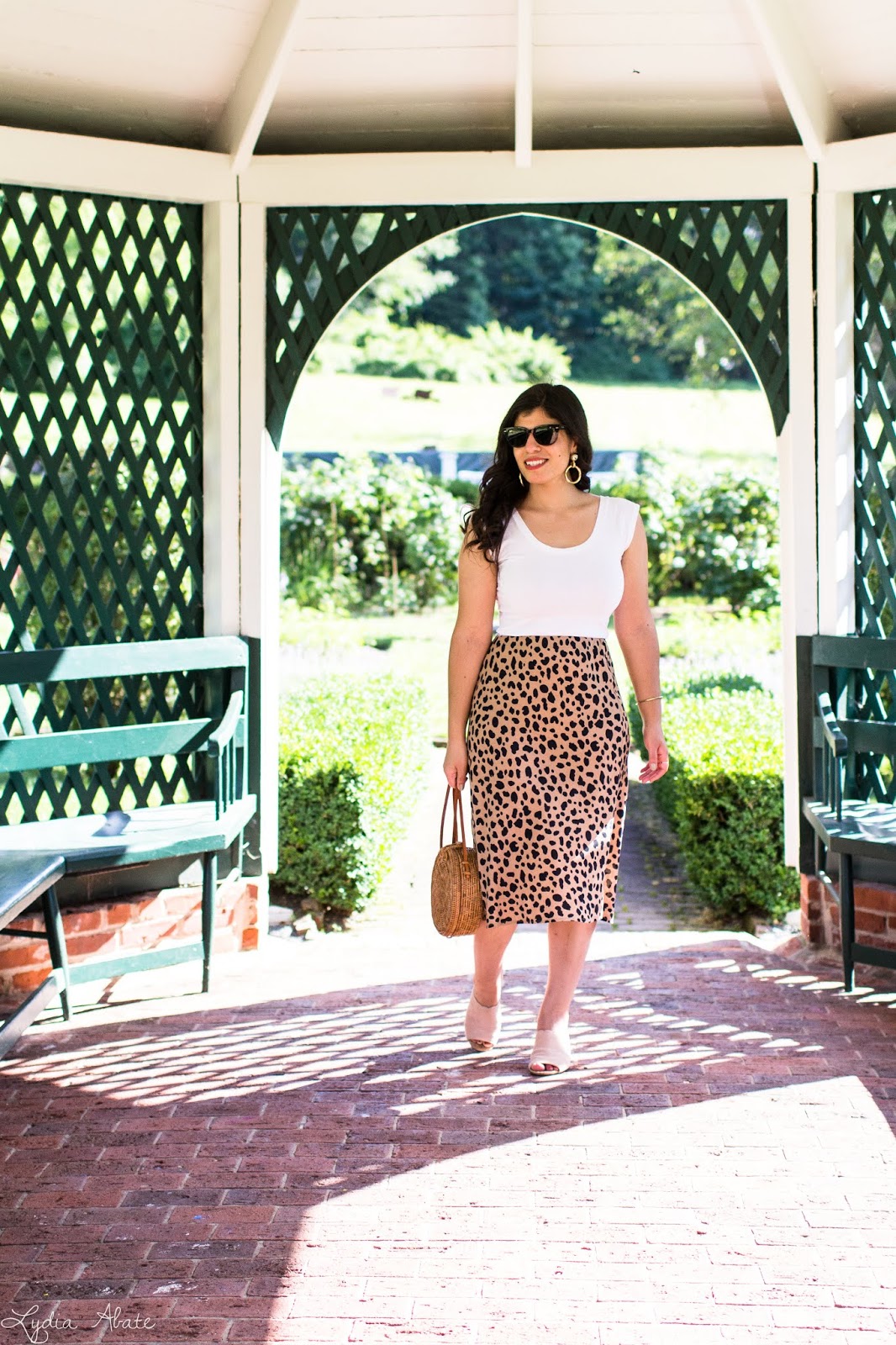 Connecticut style blogger Lydia Abate wearing a leopard midi skirt, white bodysuit, blush scalloped mules, round rattan bag, and gold hoop earrings for summer in New England