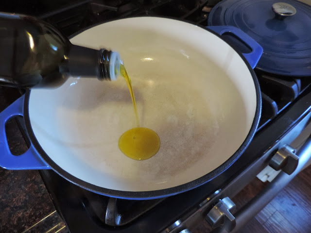 A large pot on the stove with olive oil being poured into it.