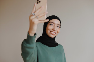 Lady wearing green long sleeved top, holding a camera above her head, while she is smiling at it