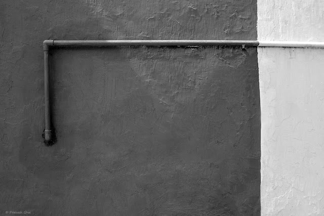 A Black and White Minimal Art Picture of a Water Pipe running across a Textured Wall. 