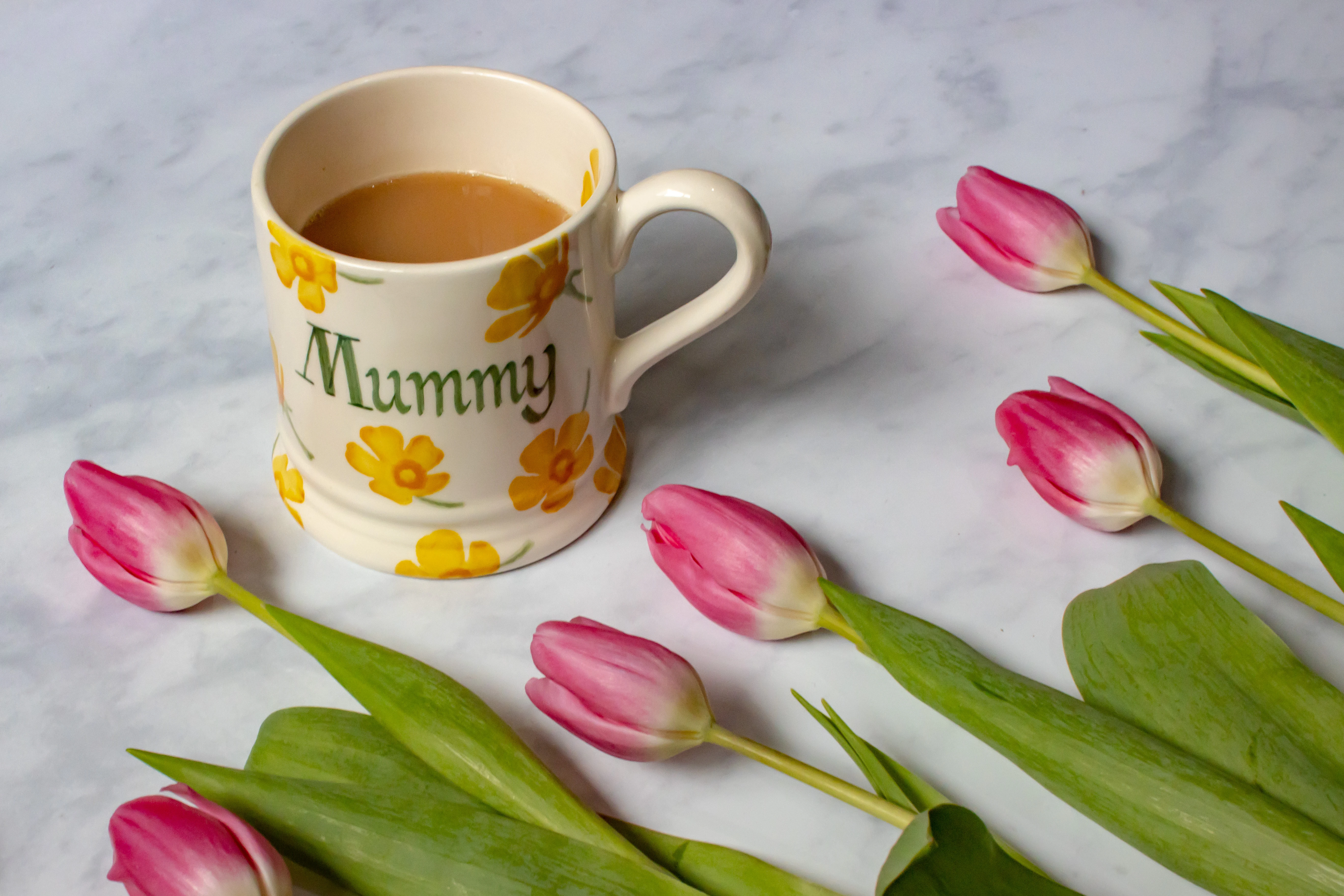 An Emma Bridgewater Mug With Yellow Flowers and saying "Mummy" next to pink tulips