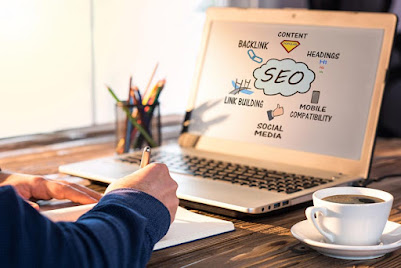 A digital marketer working on SEO on a computer with notepads, pencils and a cup of coffee on the table.