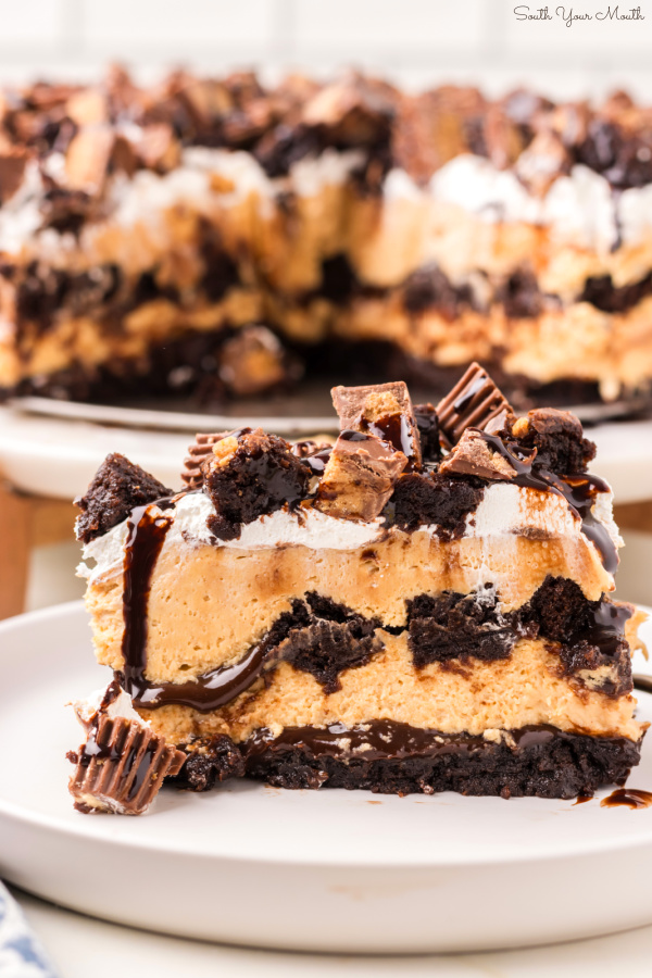 Peanut Butter Buckeye Brownie Cheesecake! An easy-to-assemble recipe with no-bake peanut butter cheesecake layered between brownie chunks and hot fudge sauce with peanut butter cups on top for a show-stopping buckeye dessert!