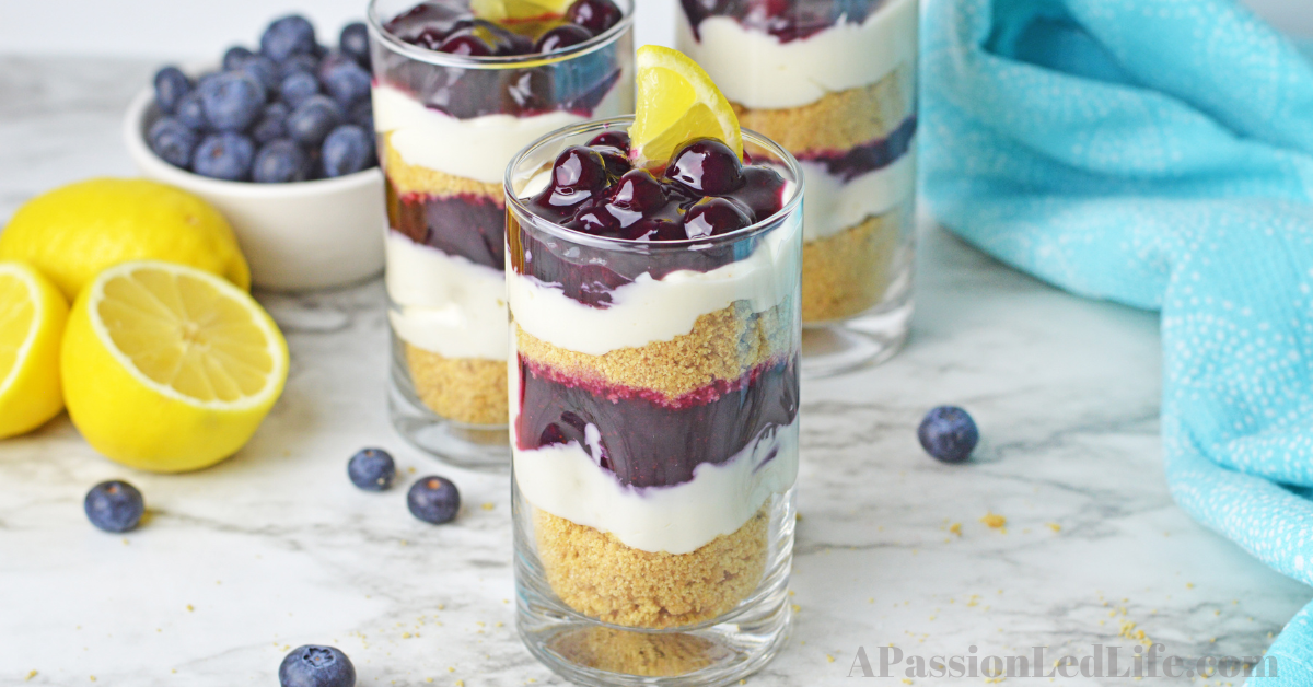 three lemon blueberry parfaits on a counter with lemons and blueberries