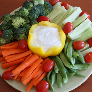 raw veggies arranged on a white plate with ranch dip in a yellow pepper