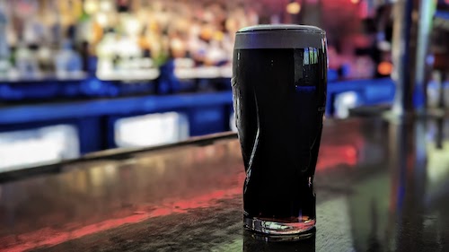 A perfectly poured Guinness sits on the bar and reflects the colorful lights