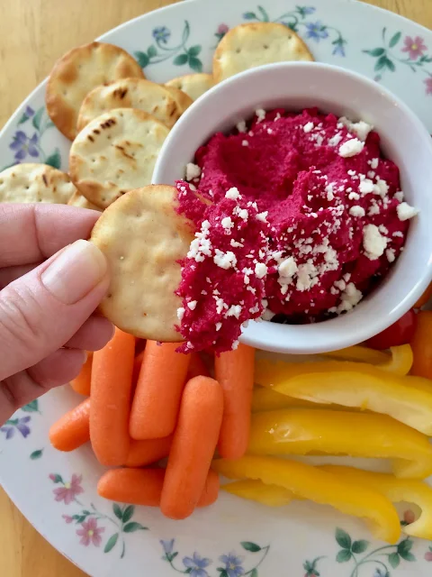 Pita cracker scooping up beet hummus with feta.