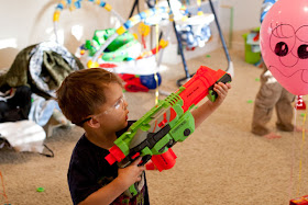 A two-year-old aiming a nerf gun at a balloon