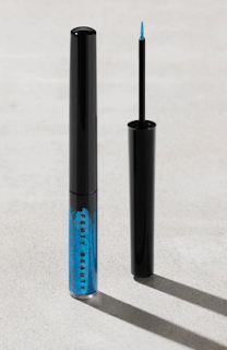 Featured is the Fenty Beauty Glitty Lid Shimmer Liquid Eyeliner in Peacocky, a dazzling blue eyeliner with fine shimmer particles. The eyeliner's sleek, slim packaging allows precision application, with a swatch on skin showing its vivid color and sparkling effect.