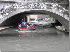 A boat passing under a pedestrian bridge on the River Walk in San Antonio, TX