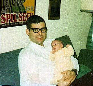 A very young dad, in black rimmed glasses, holding me as an infant.