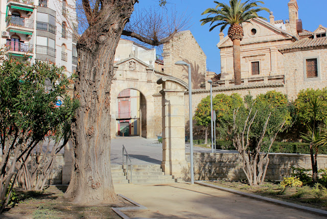 widok ze ścieżek Parku Alameda na zabytkową Bramę Anioła i barokowy klasztor klarysek, drzewa pomarańczy i palmy     