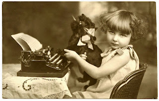 Vintage, sepia photo of a young girl and a plush toy cat at a typewriter.  