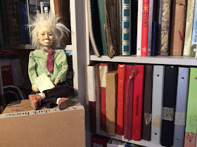 puppet Johnny Dwyer by Corina Duyn sitting on a box in front of bookshelf 