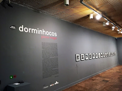 Parede com texto sobre a exposição e ao lado algumas fotos