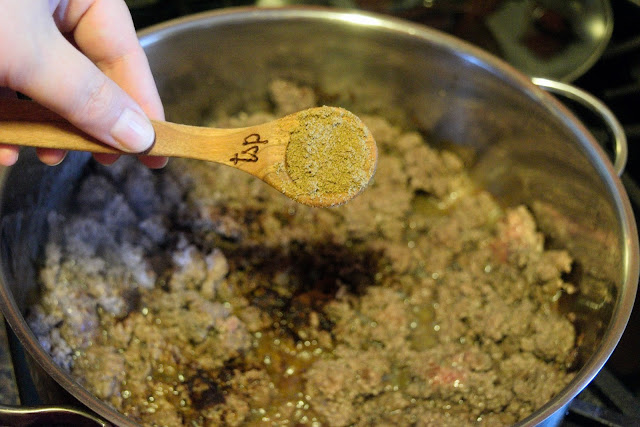 Cumin being added to the cooked ground beef in the skillet.