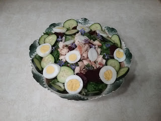 A large transferware bowl filled with lettuce, round slices of hard-boiled egg, cucumbers and boiled beets around around the edges, and accented with small blue flowers.