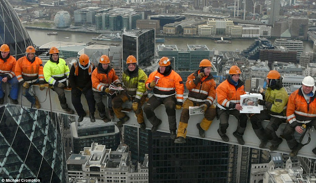 Eleven workers wearing helmets and sitting on the beam on the skyscraper in central London