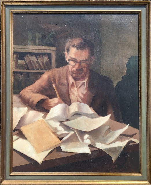 Oil painting of a man working at desk with book and many papers scattered in foreground. He wears a brown jacket, glasses, and is writing with a yellow pencil.