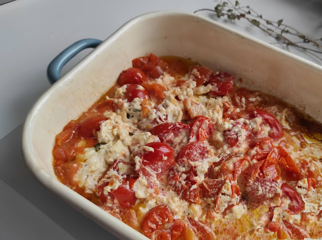 Foto di una teglia da forno con dentro dei pomodorini rossi e un panetto di formaggio feta, condito con origano olio e aglio