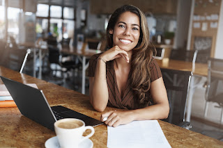 Foto de mulher sorrindo sentada a mesa com notebook em frente a ela
