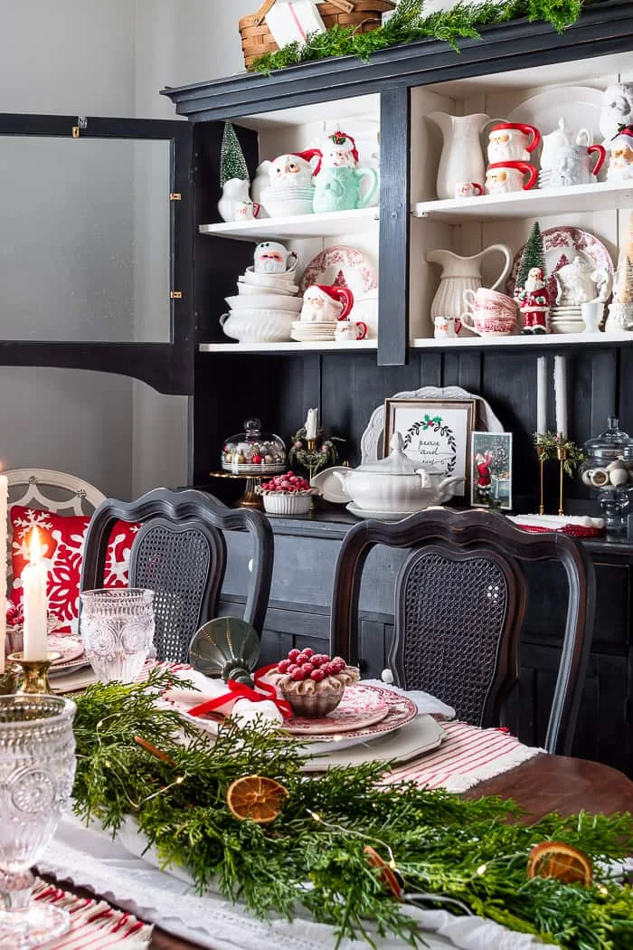 black hutch with white ironstone, vintage Santa mugs, table decorated for Christmas