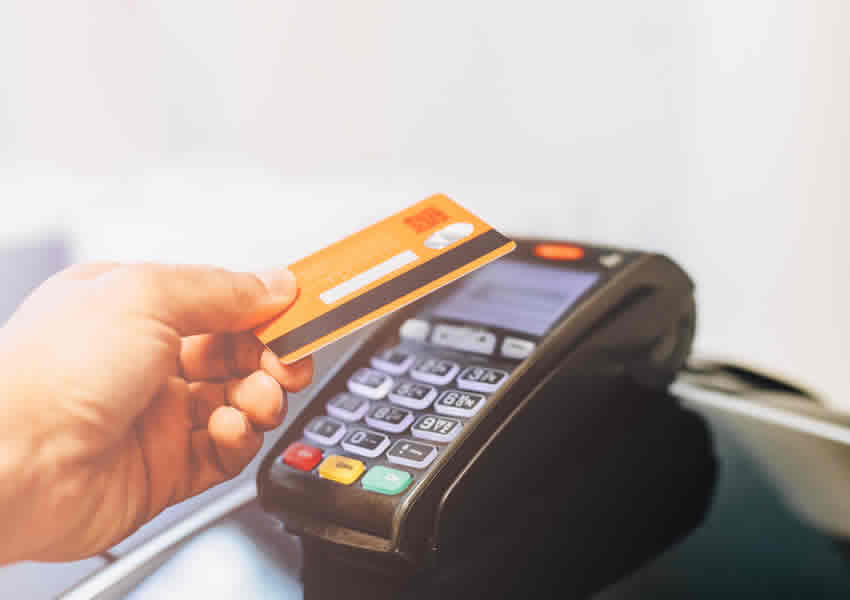 Imagem mostra uma mão fazendo o pagamento com cartão de crédito usando o contactless em uma maquina de cartão de crédito.