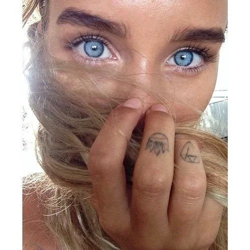 Imagen espectacular en primer plano de la mirada azul celeste de una chica, vemos en sus dedos tatuajes pequeños