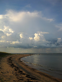 Harjusaaren kapea hiekkainen niemi, jota ympäröi meri. Taivaalla on sadepilviä.