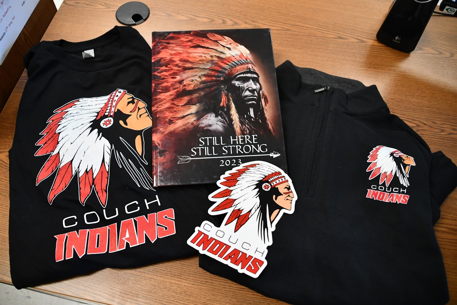 Couch Indian logo branded items on table, including shirts, stickers, yearbook