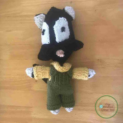 Picture of a knitted black cat soft toy wearing a yellow jumper and green overalls