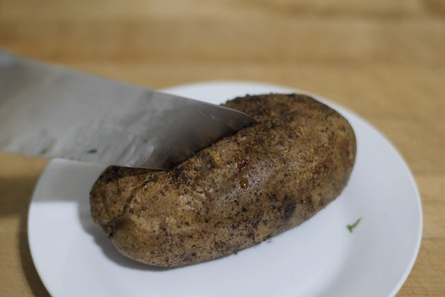 A knife cutting a slit in the top of the potato.  