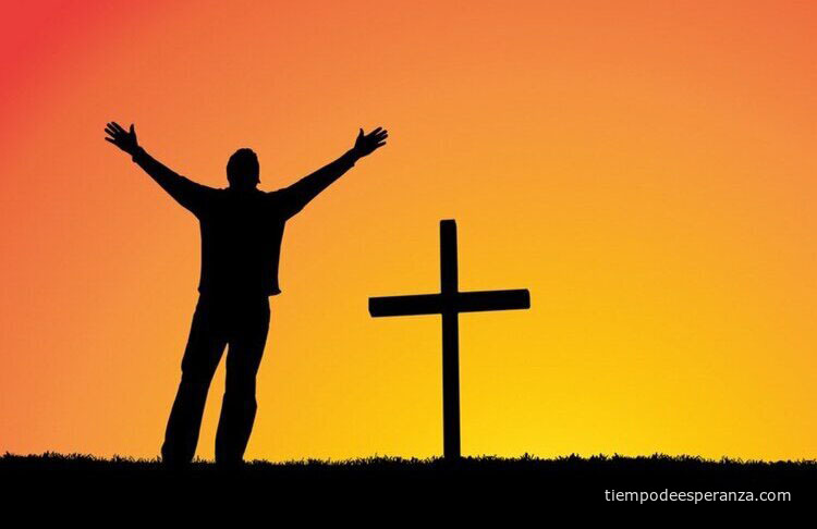 Hombre manifiesta su fe levantando las manos ante una cruz