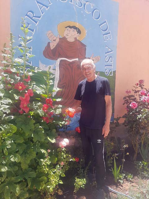 Foto: Der Padre vor dem Bild des heiligen Franziskus welches von Blumen gesäumt ist