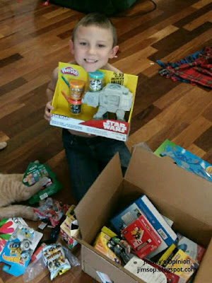 our grandson Benjamin holding a Play Doh set sitting behind the box of christmas goodies we mailed to him.