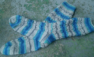 A pair of fingering-weight lace socks done up in striping sock yarn.   Yarn stripes between tan, grey, light teal, and royal blue.