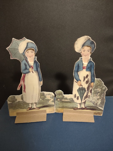An old-fashioned paper doll is shown in two similar outfits, one clean and the other spotted with mud.