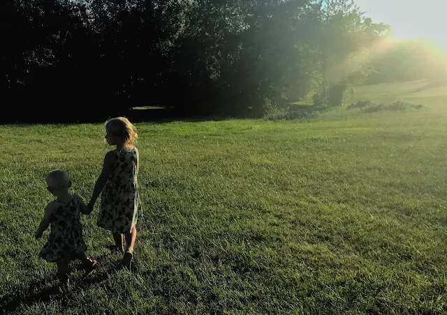 Two young girls walking hand in hand away from the camera partially silhouetted by the setting sun